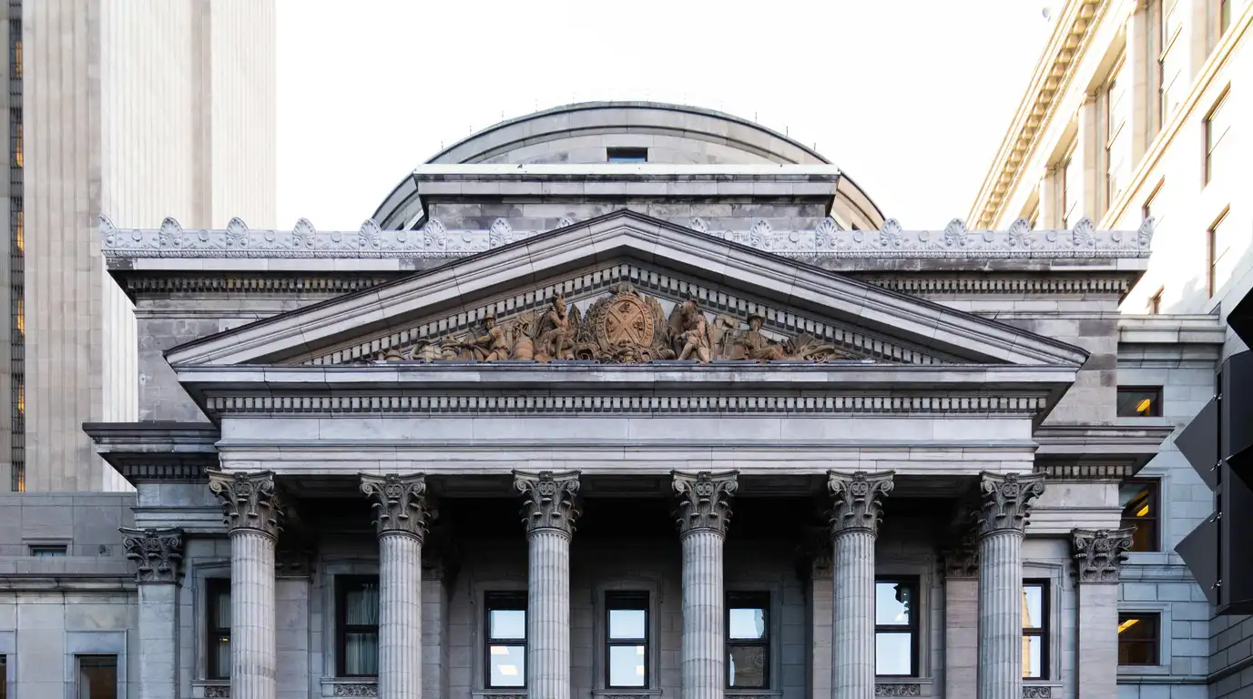 Grey stone facade with Corinthian columns, a sculpted pediment and a shallow dome rising against a white sky.