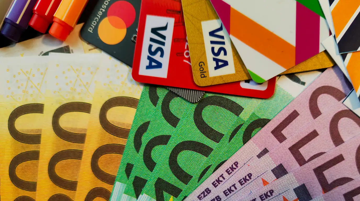 Payment cards fanned over overlapping euro banknotes in yellow, green and pink, with marker pens at the top edge.
