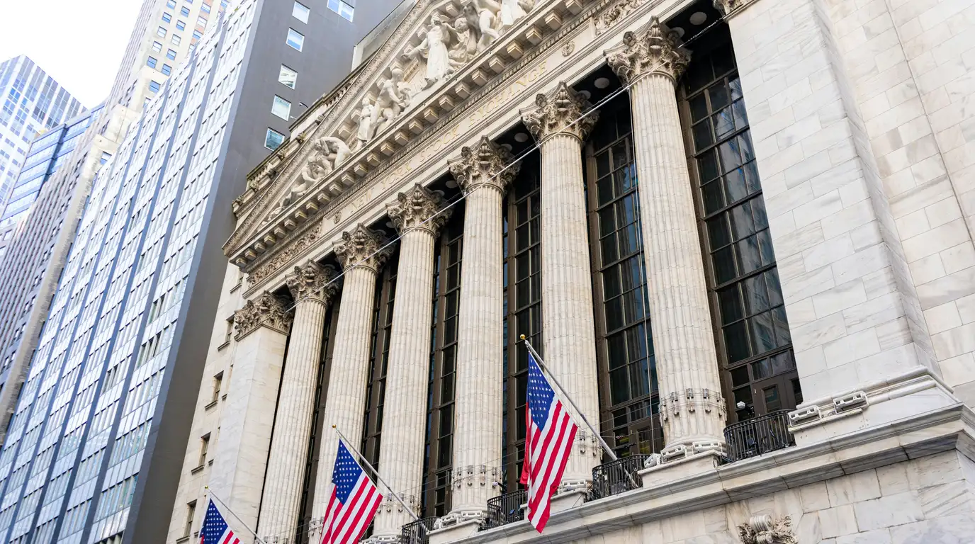 A neoclassical stone facade with Corinthian columns and pediment sculpture, three American flags hanging above the street.