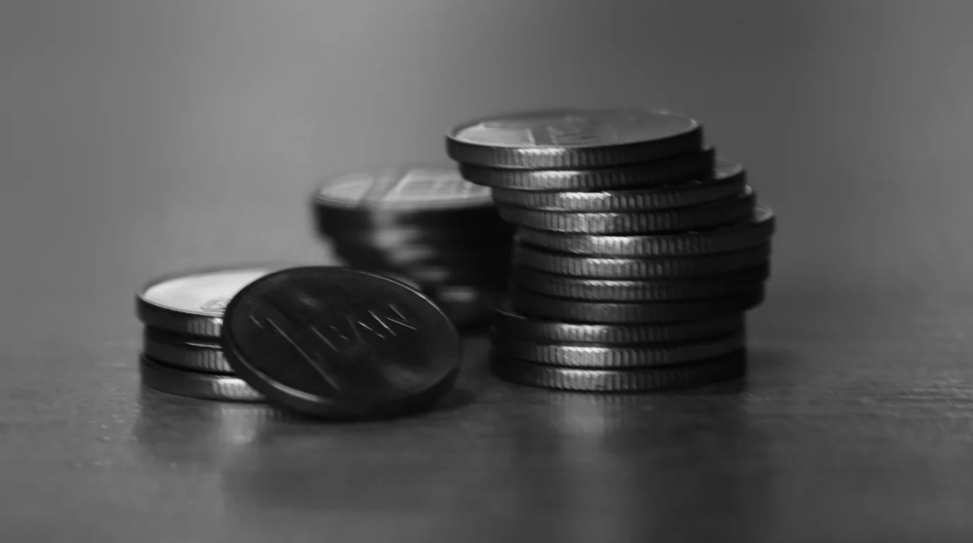 Black-and-white close-up of small coin stacks on a smooth dark surface, one coin propped on its side at the front.