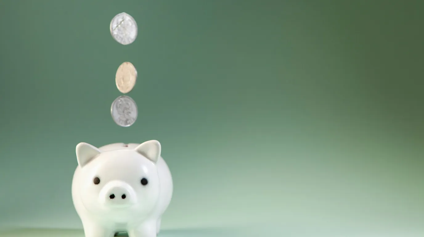 Coins dropping into a white piggy bank against a green background.